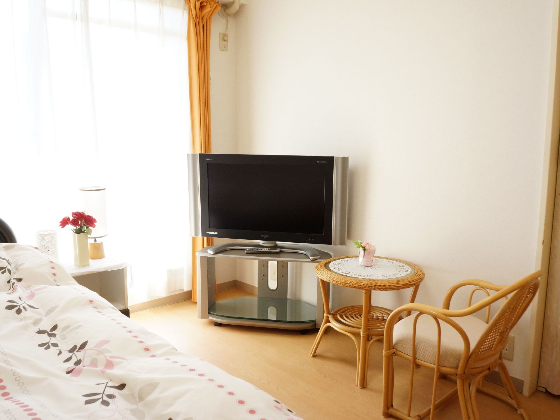 ベッドの他、テレビ、籐のテーブルと椅子が置かれている。枕元には低い台があり、花瓶に生けられた花と照明がある。