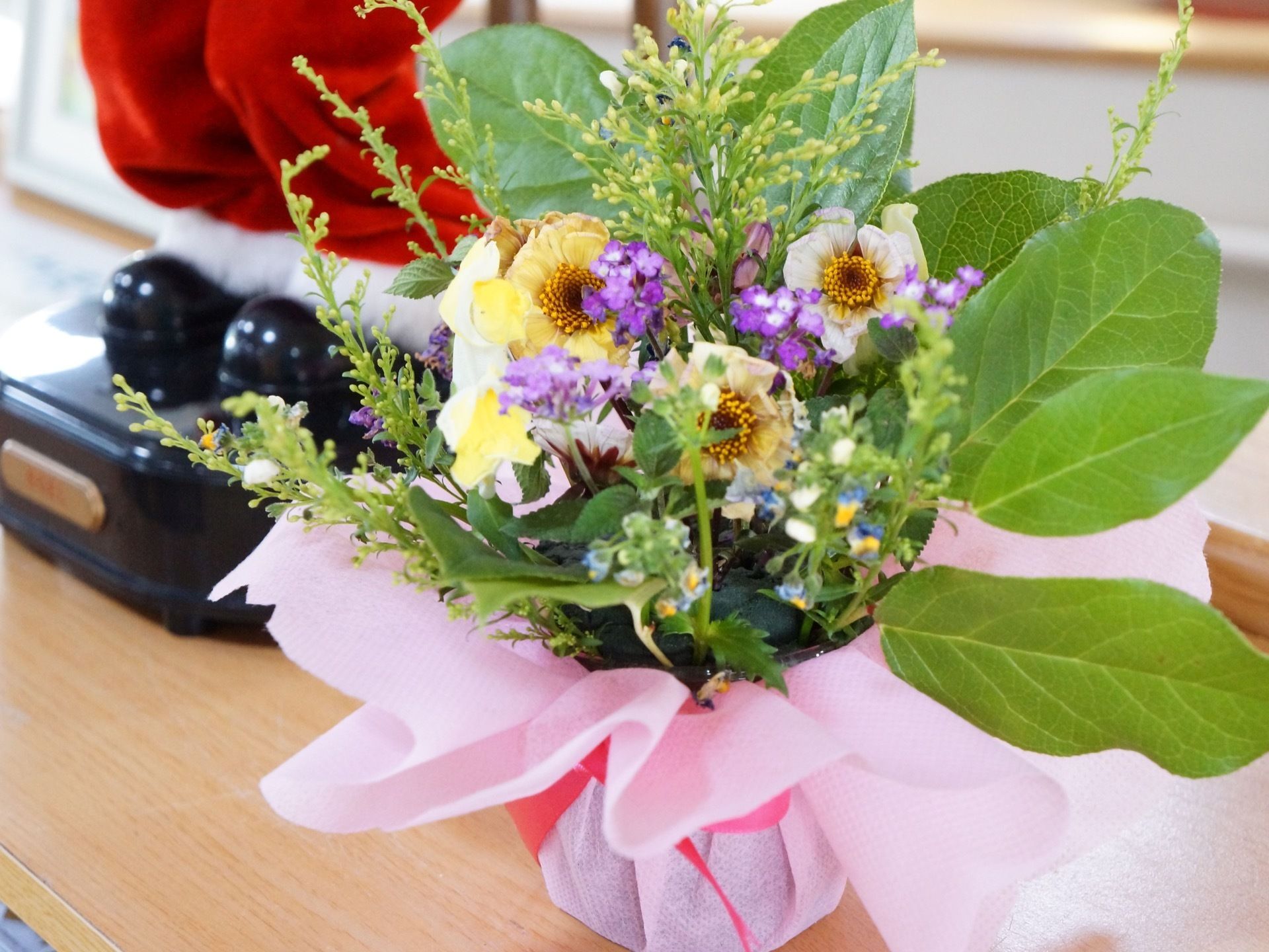ピンク色の布で可愛くラッピングされた植木鉢が置かれている。黄色紫青と綺麗な花が咲き、青々とした緑の葉がある。