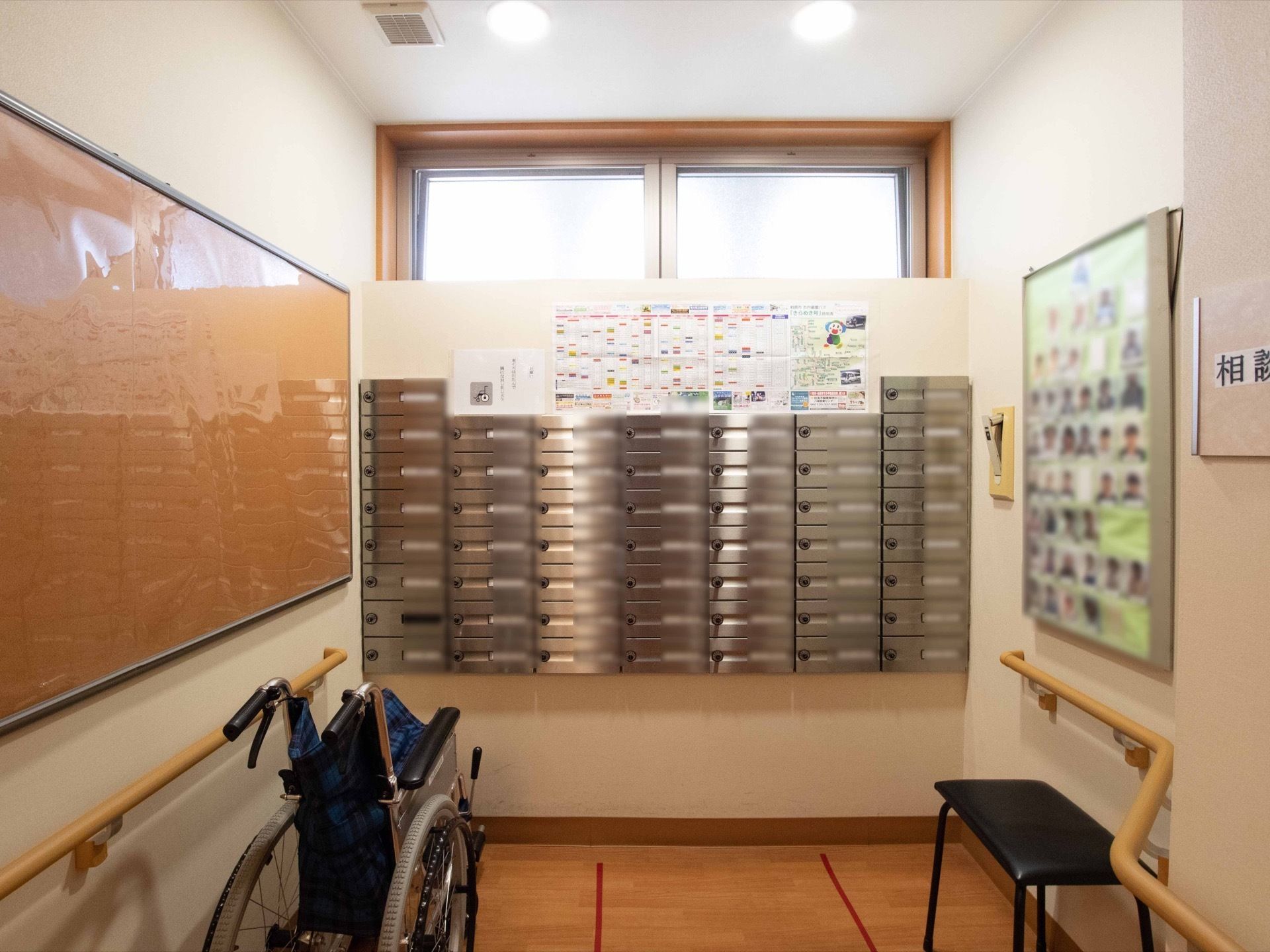 入居者様ごとのポストが壁に設置されている。掲示板に入居者様やスタッフの顔写真が掲示されている。折り畳みの車椅子が置かれている。