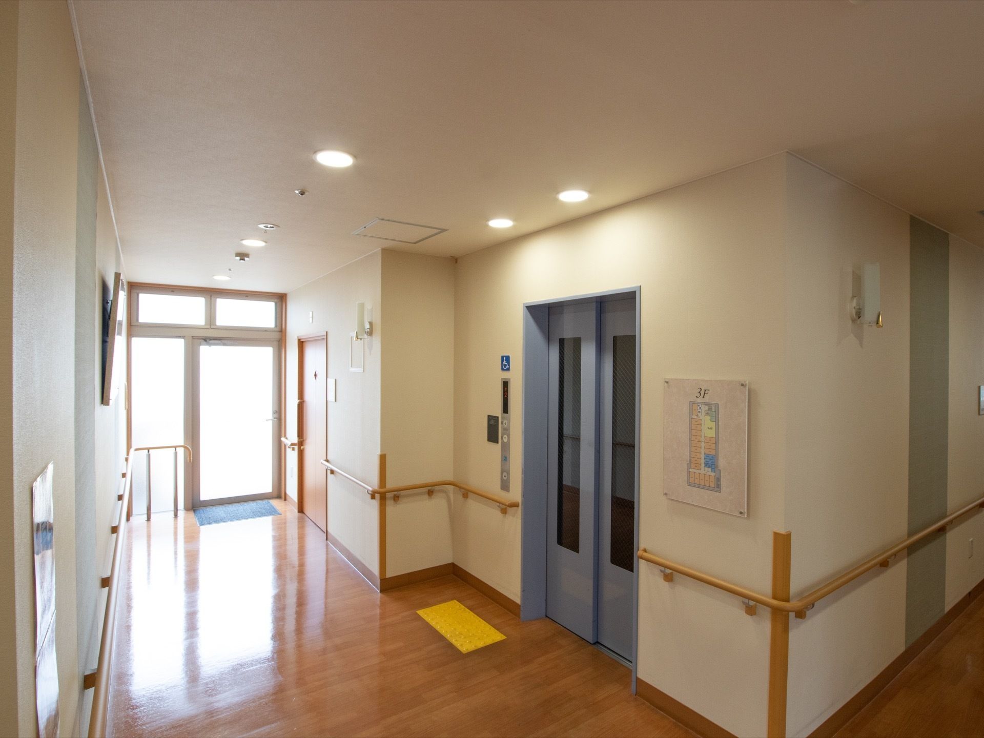 エレベーターの扉横には各階のフロアの案内図や、絵画の額縁が貼られている。突き当りは非常口になっている。