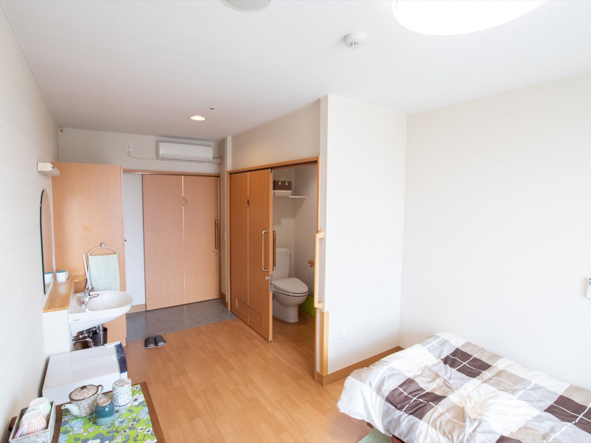 居室各室にトイレと洗面台を完備している。エアコンが入口扉上に設置されている。ベッドが壁際に置かれている。