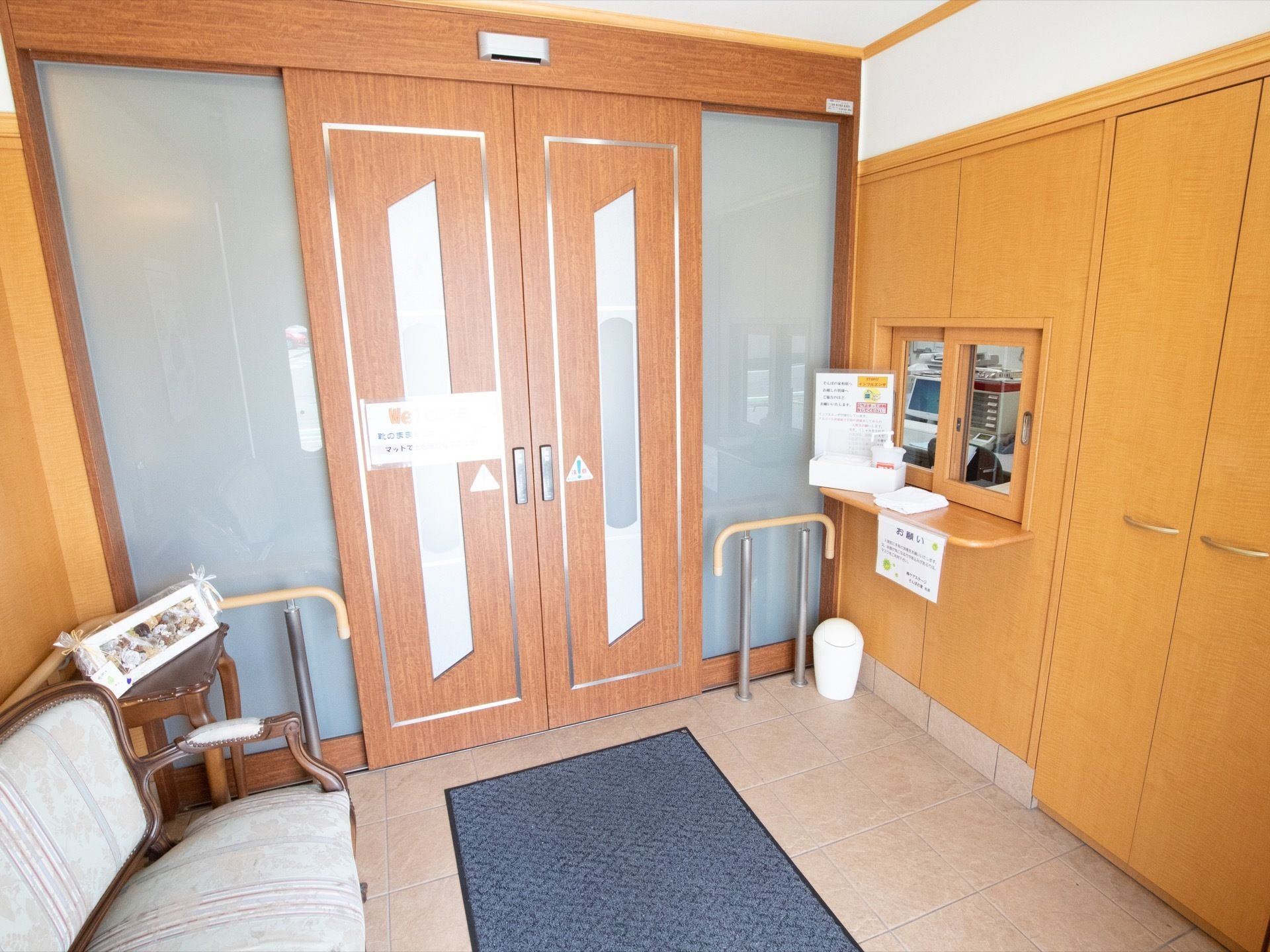 施設に入るとスタッフが24時間スタッフが常駐している事務室と繋がる窓がある。ごみ箱と椅子が置かれている。