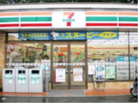 施設の近くにあるコンビニの店舗の正面外観である。入口の自動ドア付近にはゴミ箱が置かれ、屋根には店名が表示されている。