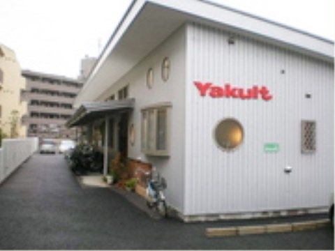 乳製品を販売する会社の建物の外観である。平屋建ての建物で、壁の色は白色系である。壁の側壁には社名が表示されている。