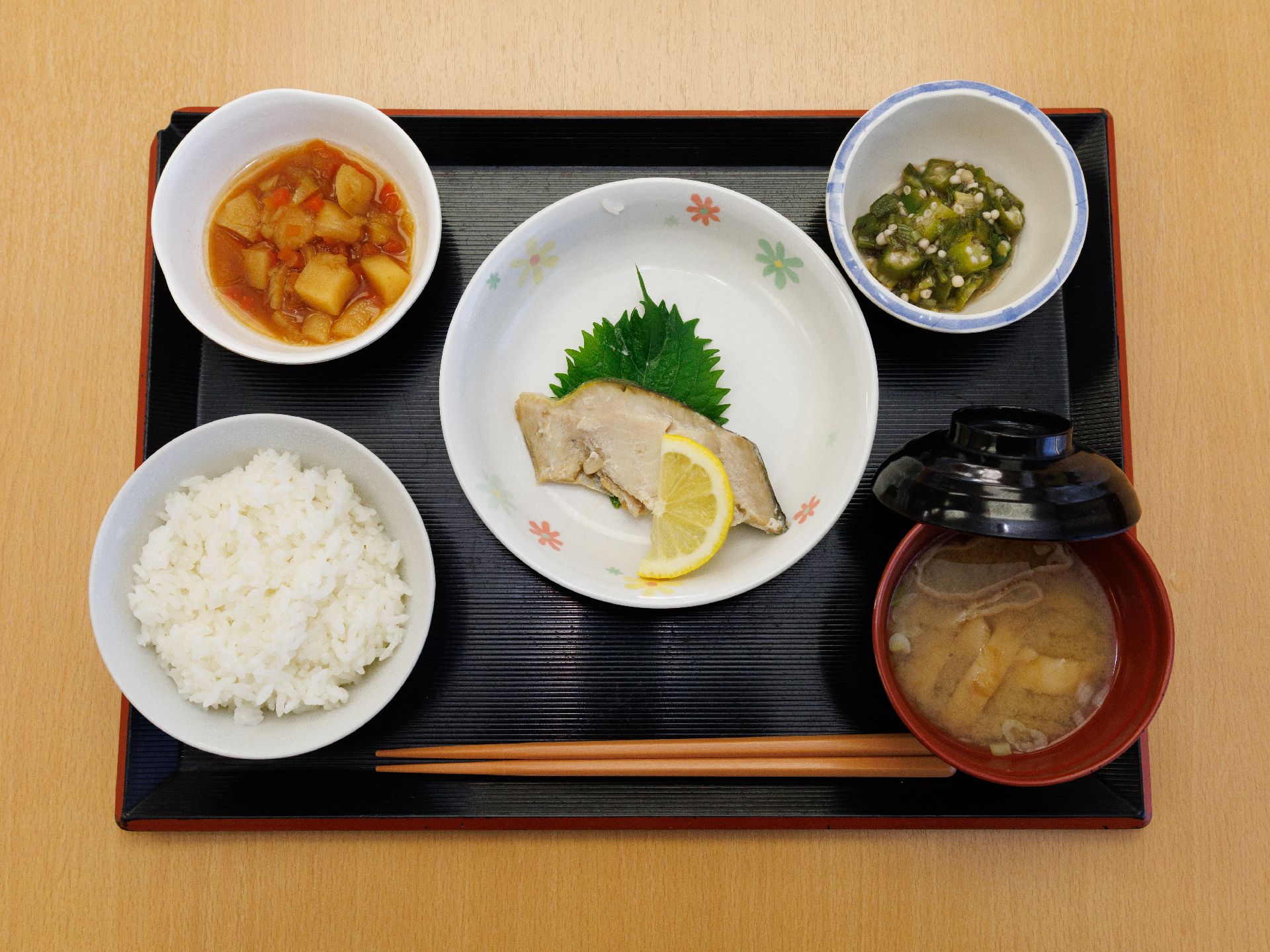 きゅうりの塩もみや魚の煮つけ、ご飯、味噌汁が並んでいる黒いお盆