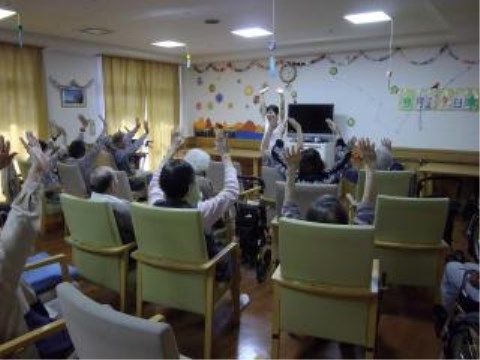 １室で指導員を前に椅子席に腰掛け、同じ動作をしている入居者様