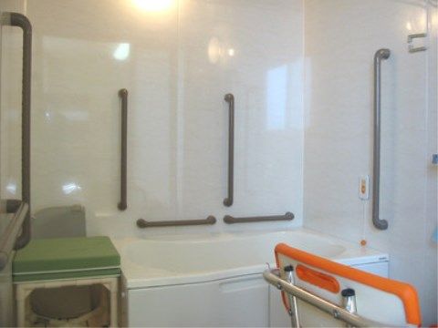 白いユニットバスが設置され、壁に手すりや緊急ブザーが取り付けられた浴室