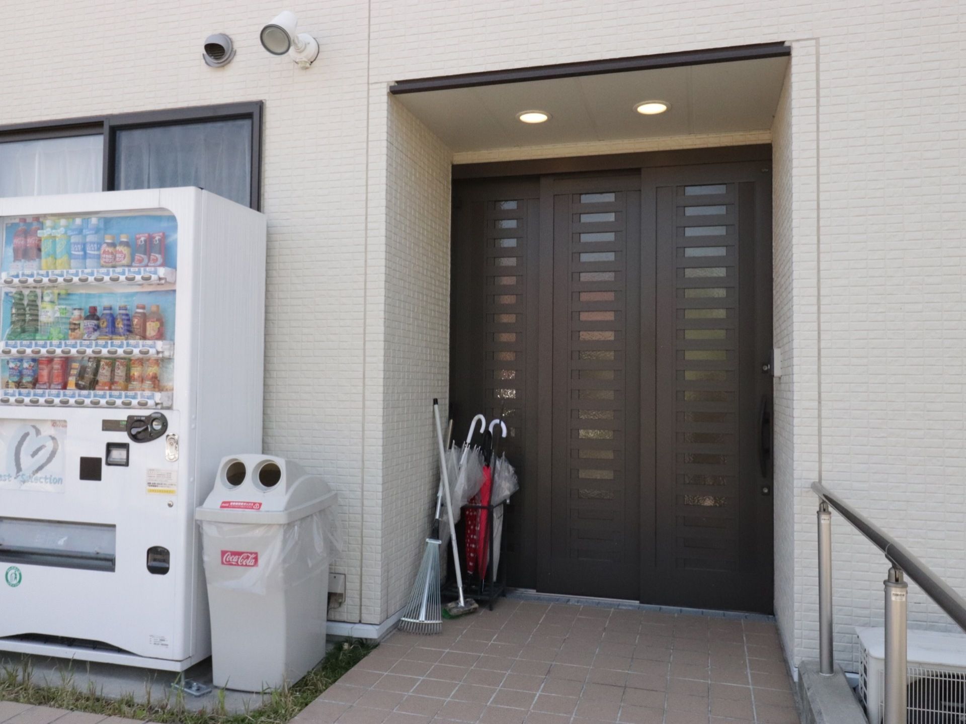 玄関は３枚の扉の引き戸となっている。入口には共同の傘立てが置かれている。自動販売機とごみ箱も設置している。