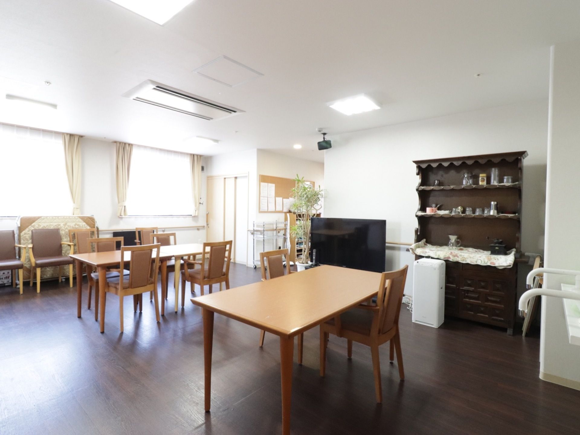 窓が大きく開きとても明るくなっている。テーブルセットが用意されている。掲示板にはグループホームからのお知らせなどが貼りだされている。