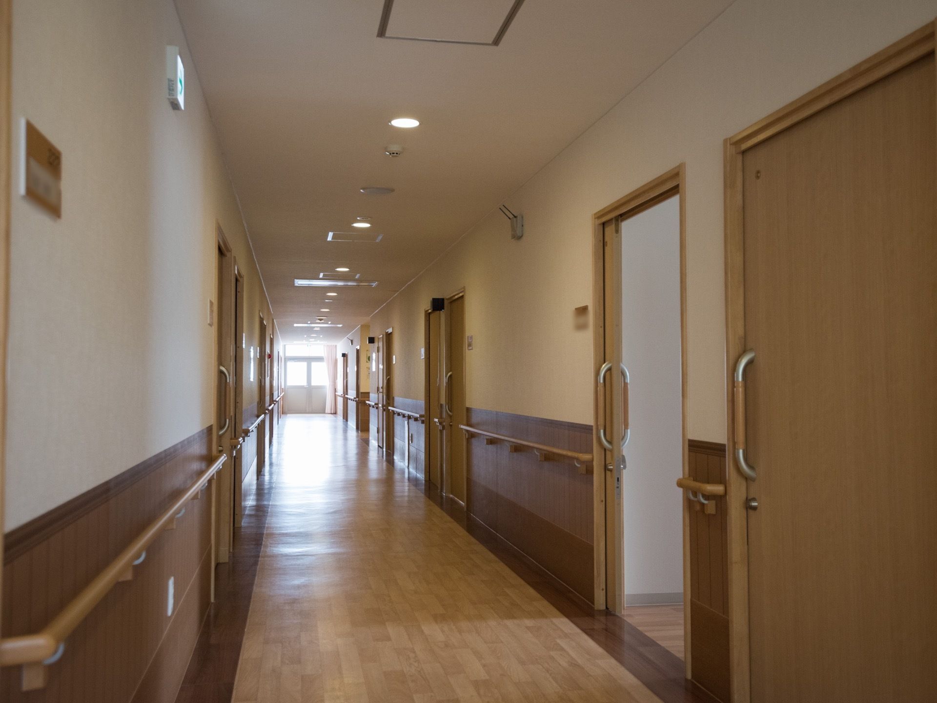 廊下の両側に居室の扉が並んでいる。扉は取っ手付きの引き戸になっていて、壁には手すりが設置されている。