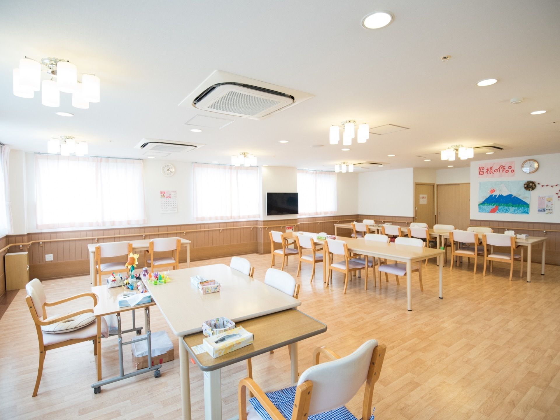 テーブルセットが並んだ広い食堂がある。天井からは洋風の照明が下がっていて、明るい空間になっている。壁にはテレビが掛けられている。