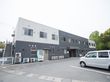 グレーと白のタイルで彩られた２階建ての建物があり、前は駐車場になっている。飲料の自動販売機が１台設置されている。