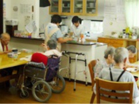 キッチンカウンターで作業中の女性スタッフ２名と食事中の入居者様