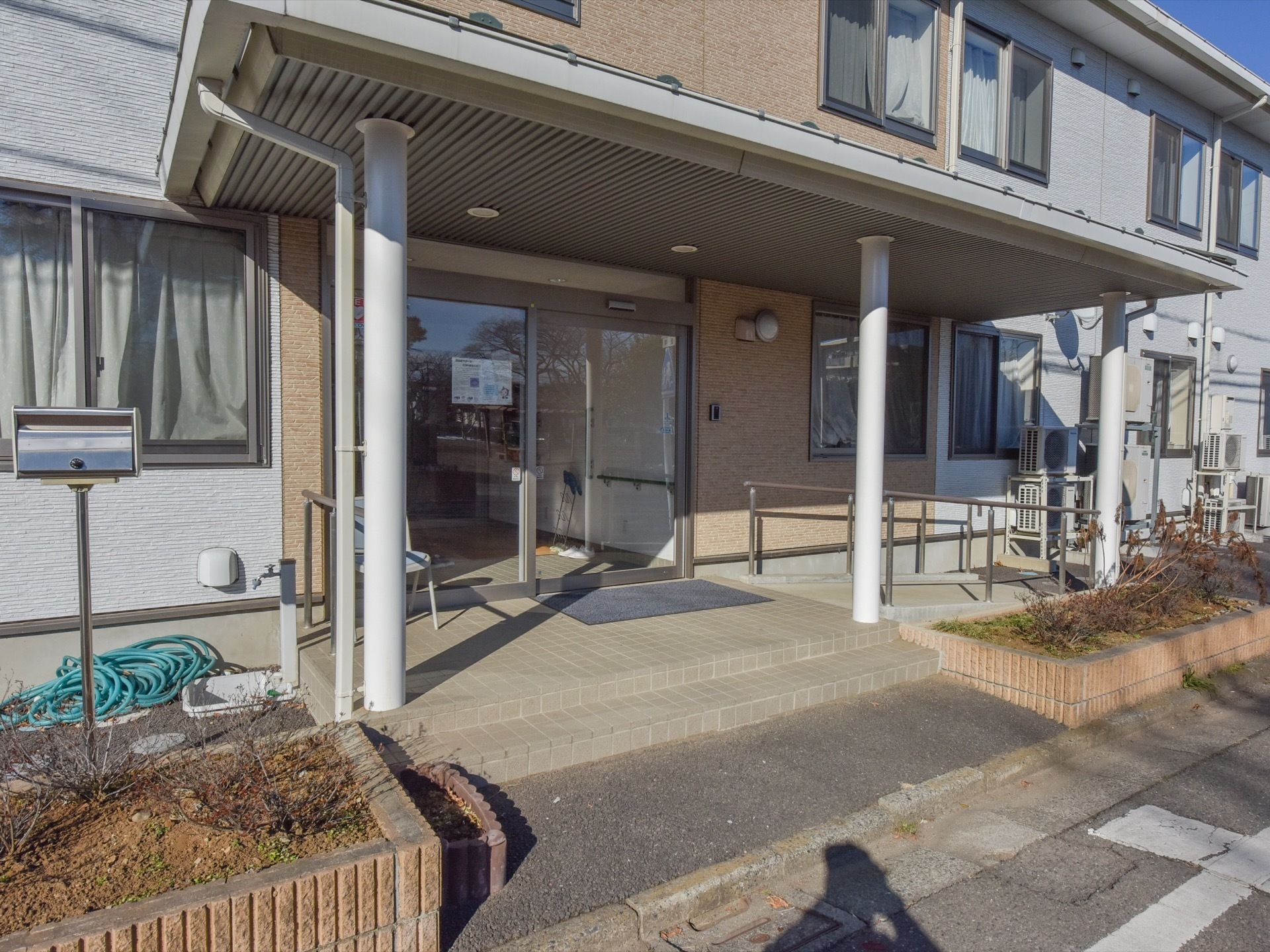 入口前には階段とスロープが設置されている。上には大きな屋根がある。建物はツートンカラーになっている。