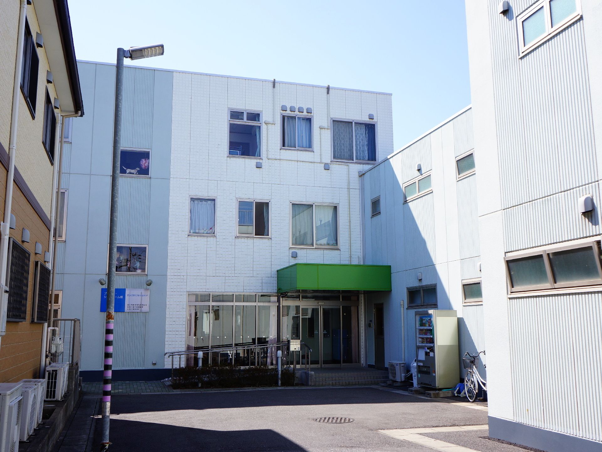 緑の屋根が付いた玄関ポーチにスロープと手すりが造り付けられた施設の外観