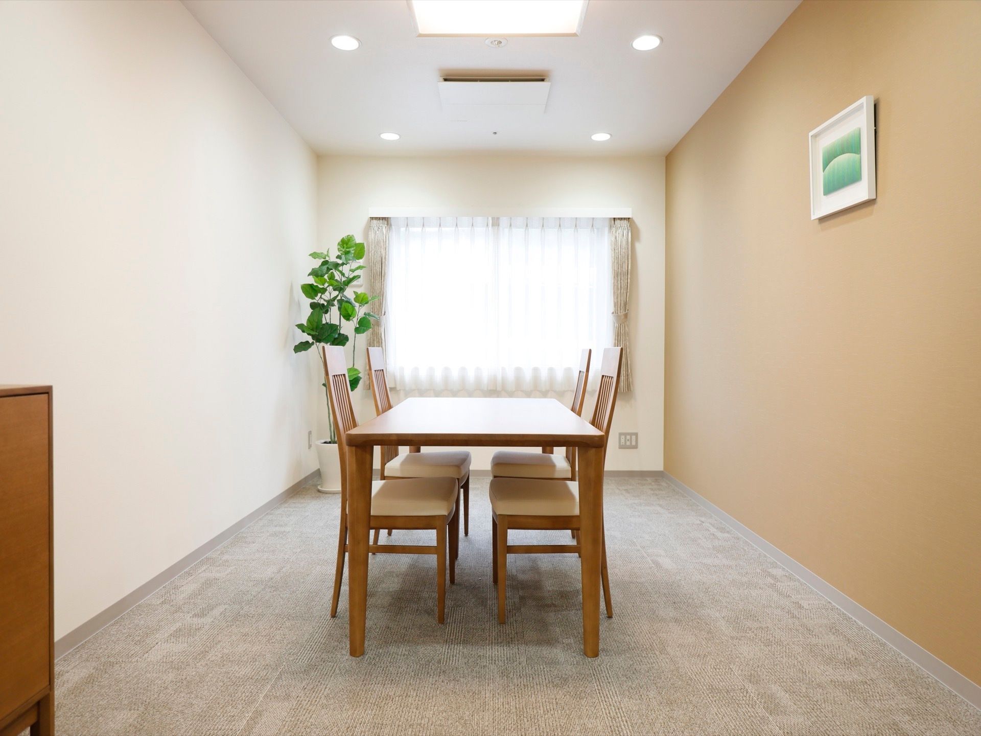 日当たりが良く明るい個室にテーブルセットが設置されている。観葉植物が置かれており、壁には絵が飾られている。