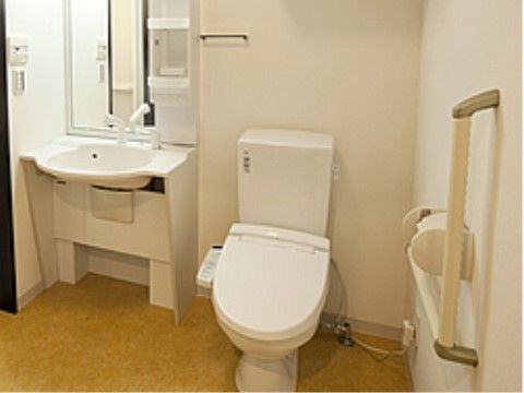 トイレ内の壁には手すりが設置されている。便座には温水洗浄便座のボタンが取り付けられている。車椅子に乗ったまま利用できる洗面台がある。