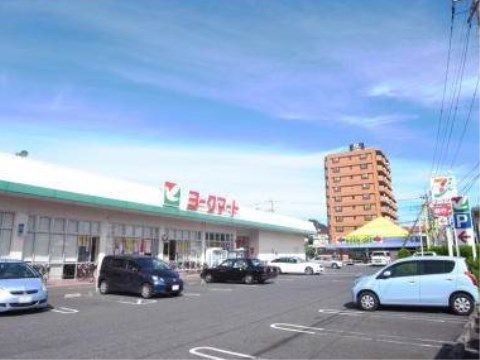 施設近隣のスーパーである。スーパーの前は駐車場になっていて何台か車が停まっている。道路側にはコンビニエンスストアの看板が見える。