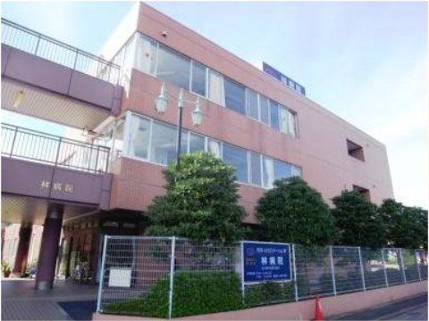 レンガ色の外壁の３階建の病院。敷地の周りには木が植えられている。入口のフェンスには病院の看板が掲げられている。