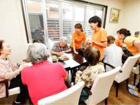 テーブルセットの椅子に腰かける複数人の入居者様皆さまと談笑する女性スタッフ