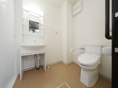 居室に洗面台と洋式便器が用意されている。洗面台には棚がいくつか設けられている。洗濯機用の水栓と排水管が設置されている。