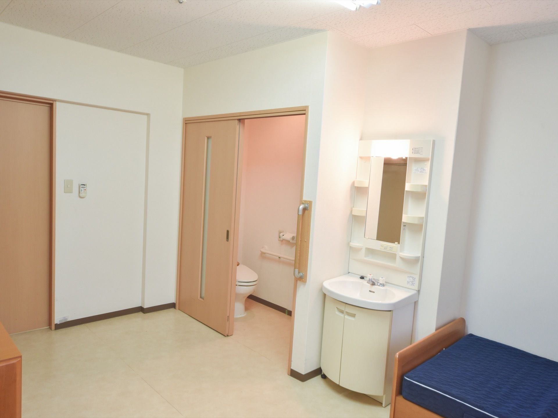 居室には洋式トイレ、洗面台、ベッドが備わっている。トイレのドアの間口は広く、外と中の壁にはしっかりした手すりが付いている。