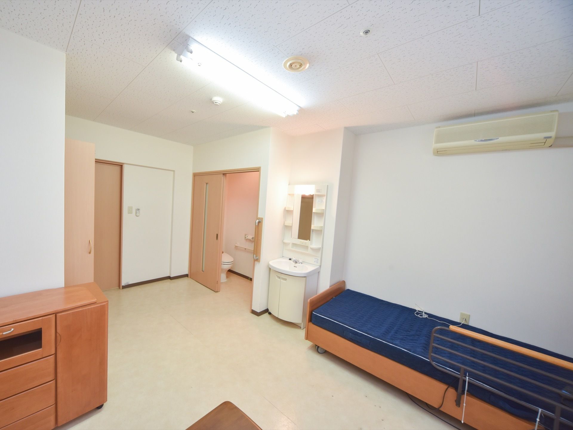 白を基調とした明るい空間。ベッド・洗面台・棚・エアコンを備えており、部屋はバリアフリー設計になっている。