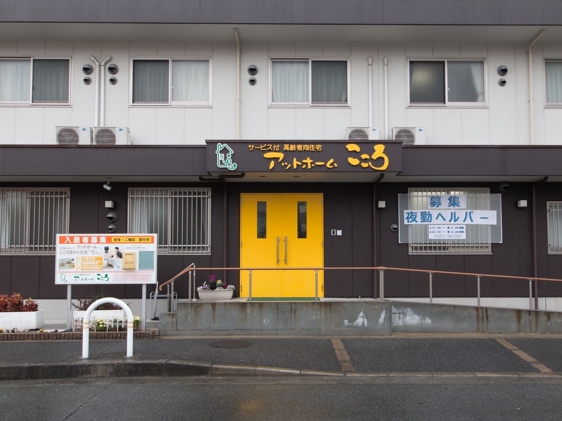 監視カメラが設置されている玄関で、１階の窓には柵が設置されている。入口のドアは両開きで、小窓がついている。