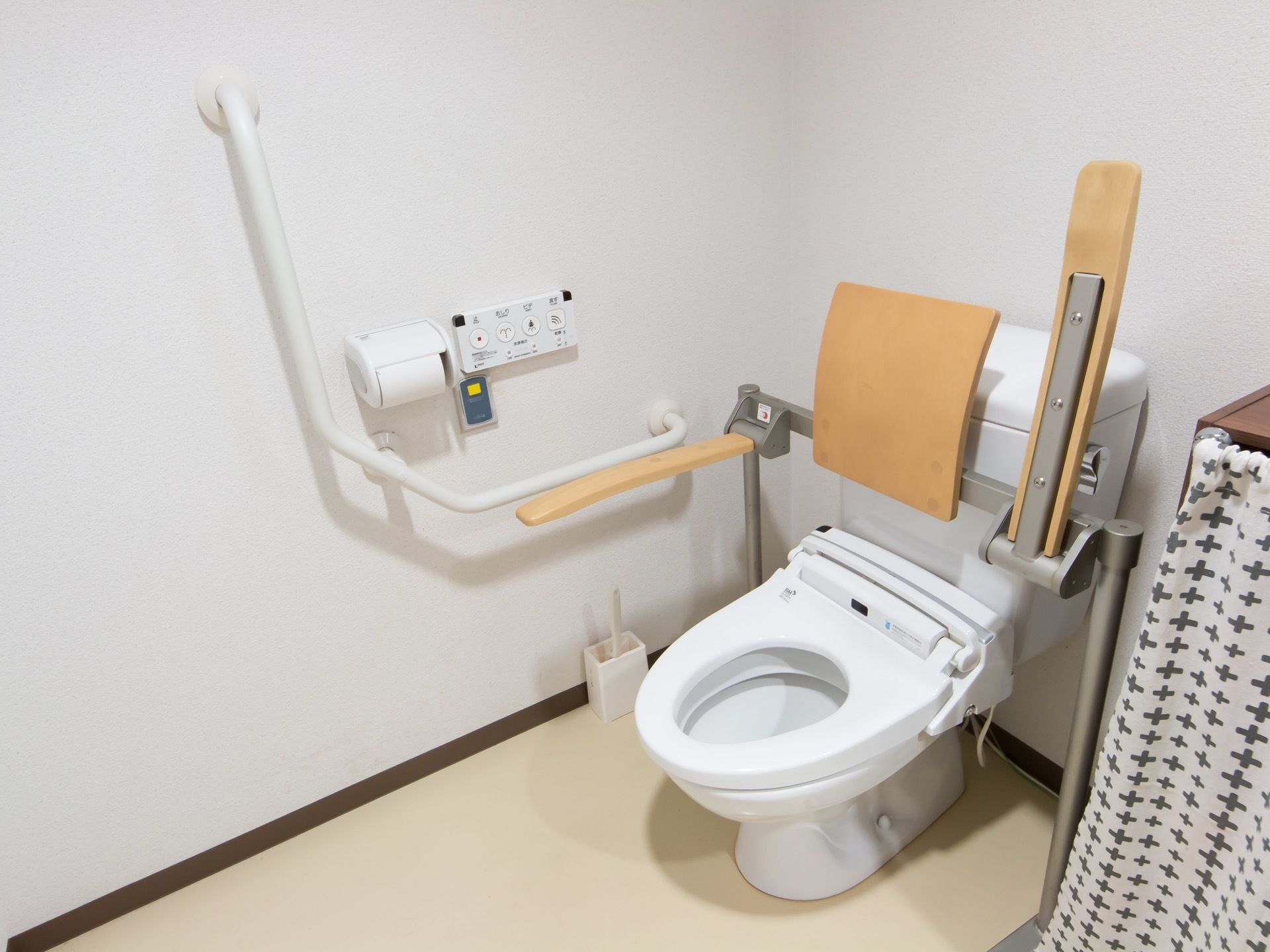 呼び出しボタンが設置されている、温水洗浄機能付きのトイレ。便座には背もたれやひじ掛けが取りつけられている。