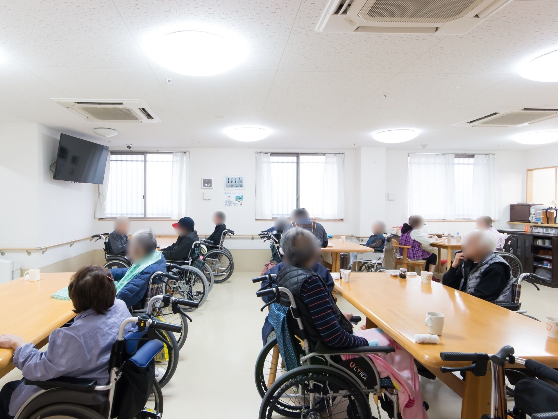 広々としたダイニングスペースに入居者様が集まっている。壁には手すりが設置されており、対面式キッチンがある。
