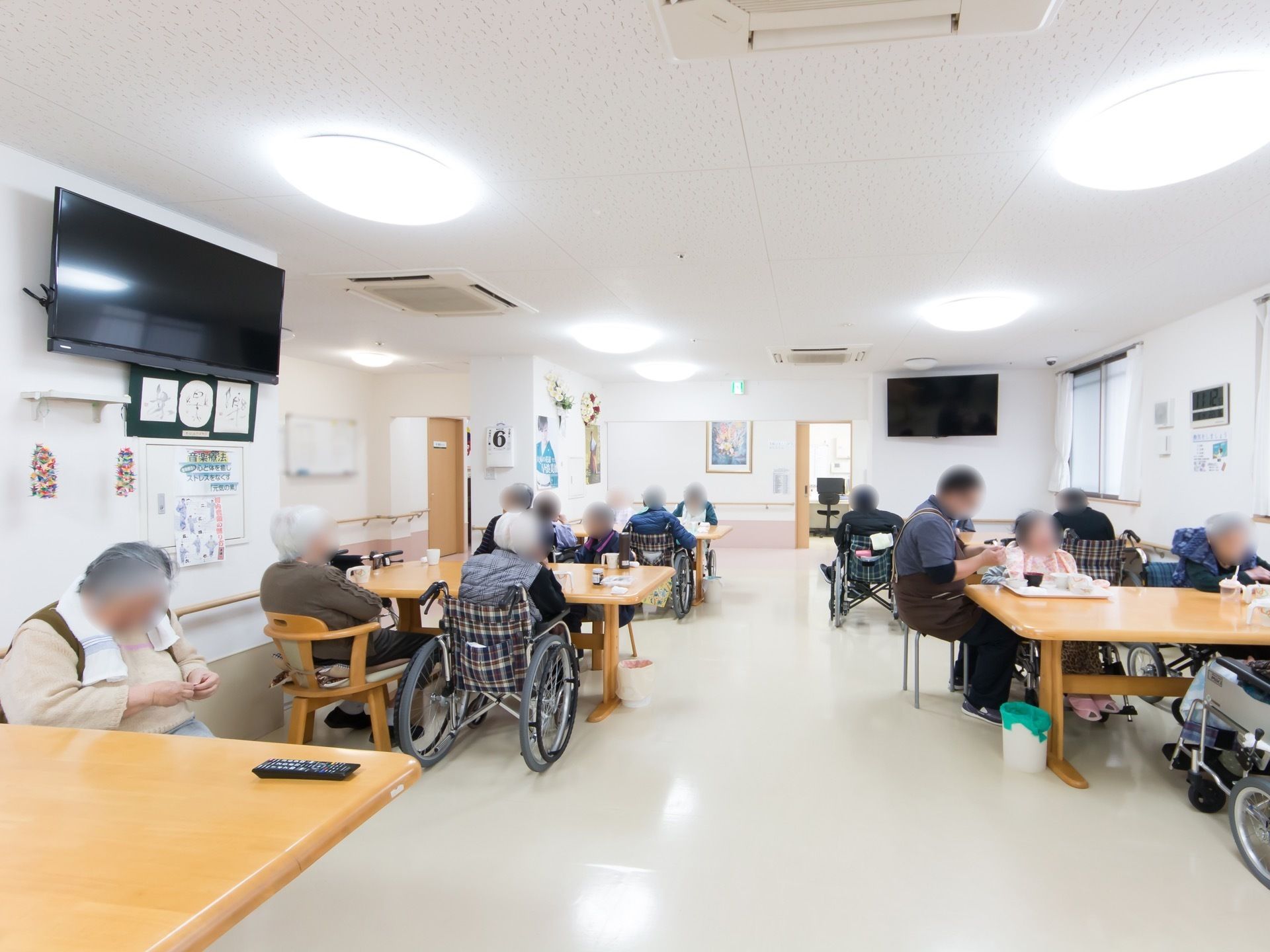 天井にたくさんの照明が取りつけられている明るい食堂。入居者様が集まり、思い思いの時間を過ごしている。
