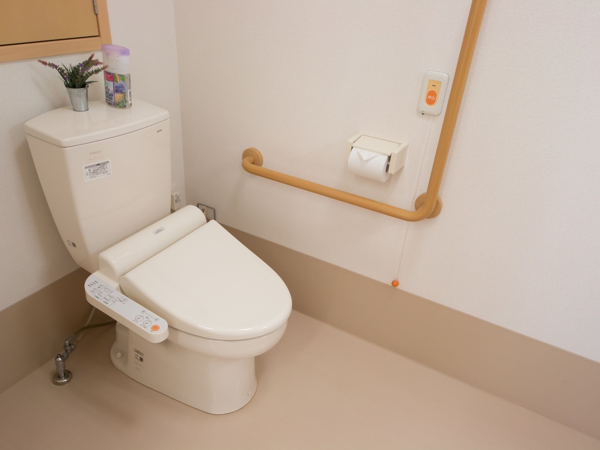 洗浄機能付きトイレが設置されている。壁にＬ字型の手すりとナースコールがつけられている。消臭剤が置かれている。