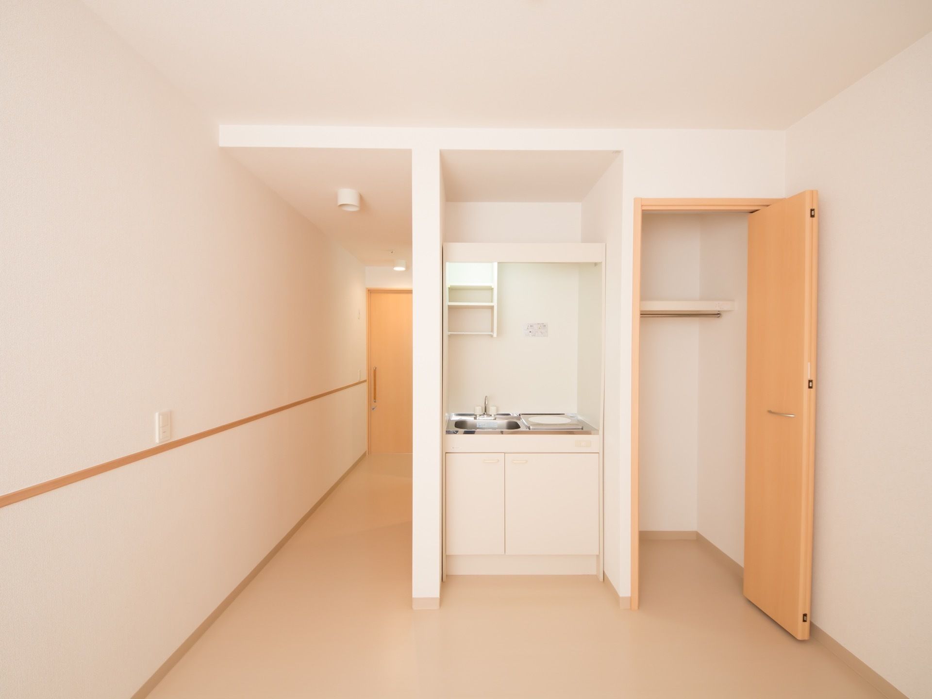 白で統一された明るい居室となっている。ミニキッチンとクローゼットが並んで取りつけられている。室内は段差のないフラットフロアとなっている。
