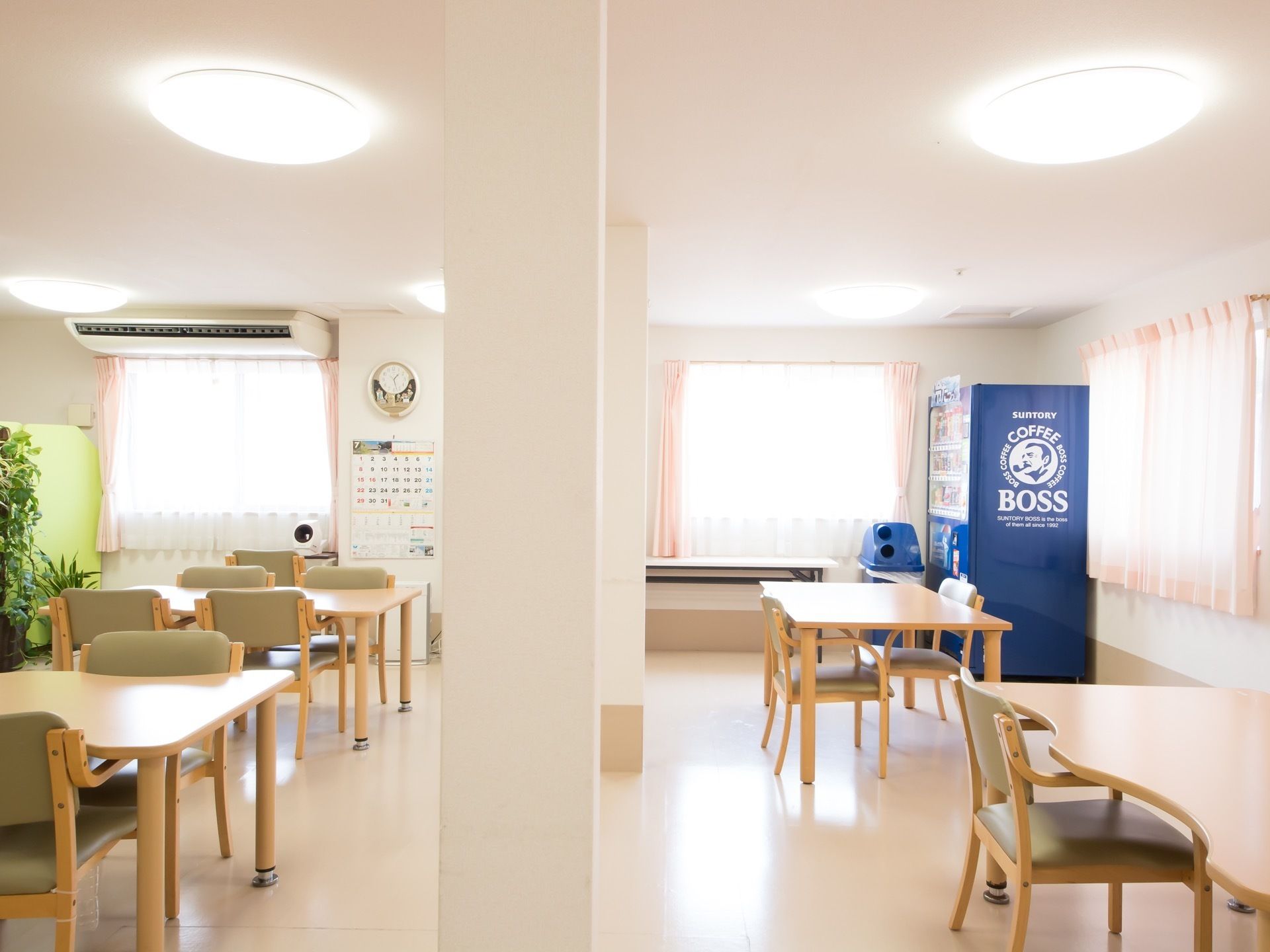日差しが差し込む明るい食堂である。ダイニングテーブルに椅子がセットされて、数組置かれている。奥には自動販売機が設置されている。