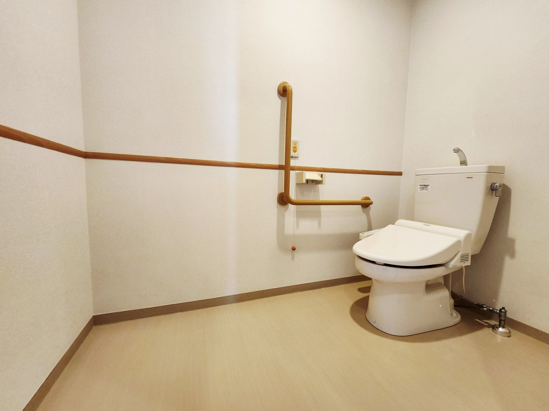 洗浄機能付きトイレが設置されている。壁にL字型の手すりとナースコールがつけられている。消臭剤が置かれている。