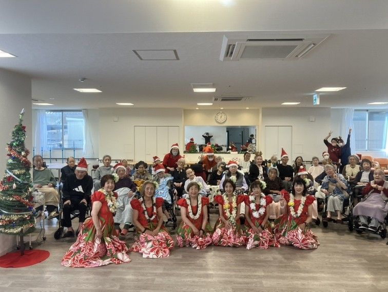 マイクを片手に微笑む女性の入居者様と手拍子する男性の入居者様、２名の女性スタッフ