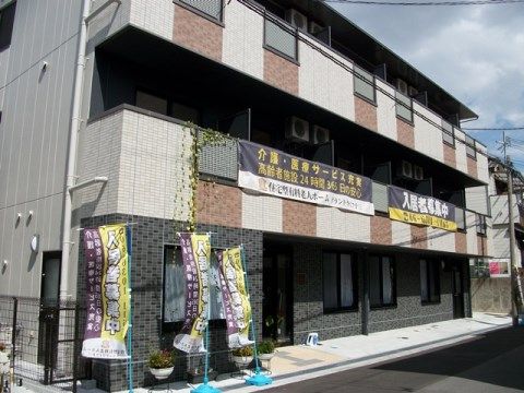 外壁に入居案内の垂れ幕を降ろした３階建て施設の外観