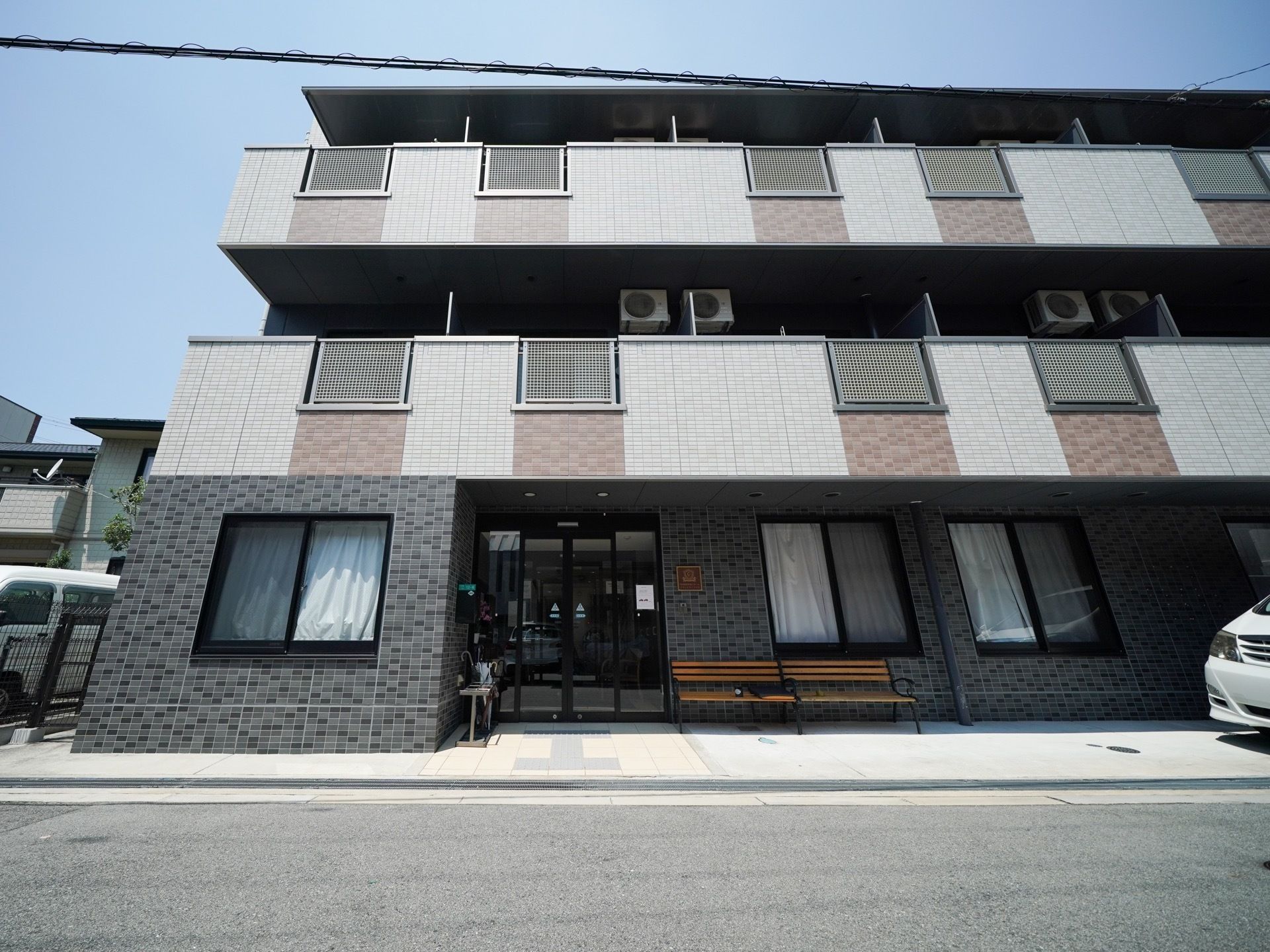 ３階建ての落ち着いた色合いのマンションのような建物である。玄関の横にはベンチや傘立てが置かれている。