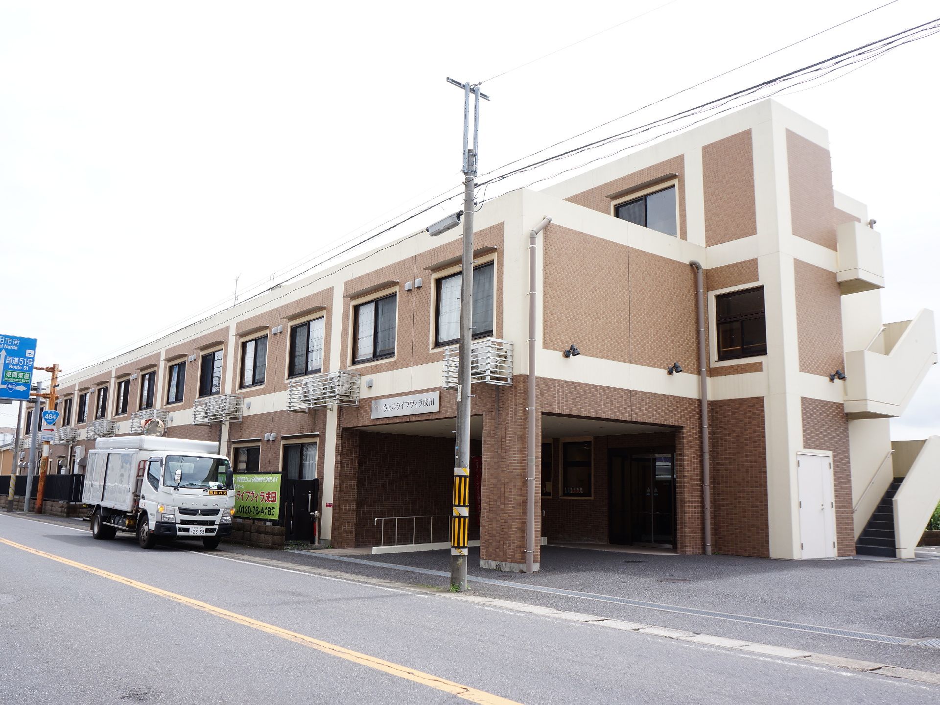 3階建ての建物の外壁はタイル張りでブラウン系の色を使用している。道路に面していて境にはフェンスが建てられている。