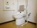 洋式トイレが設置されている。トイレにはひじ掛けと背あてが追加されている。壁にはトイレの操作パネルとL字の手すりが付いている。