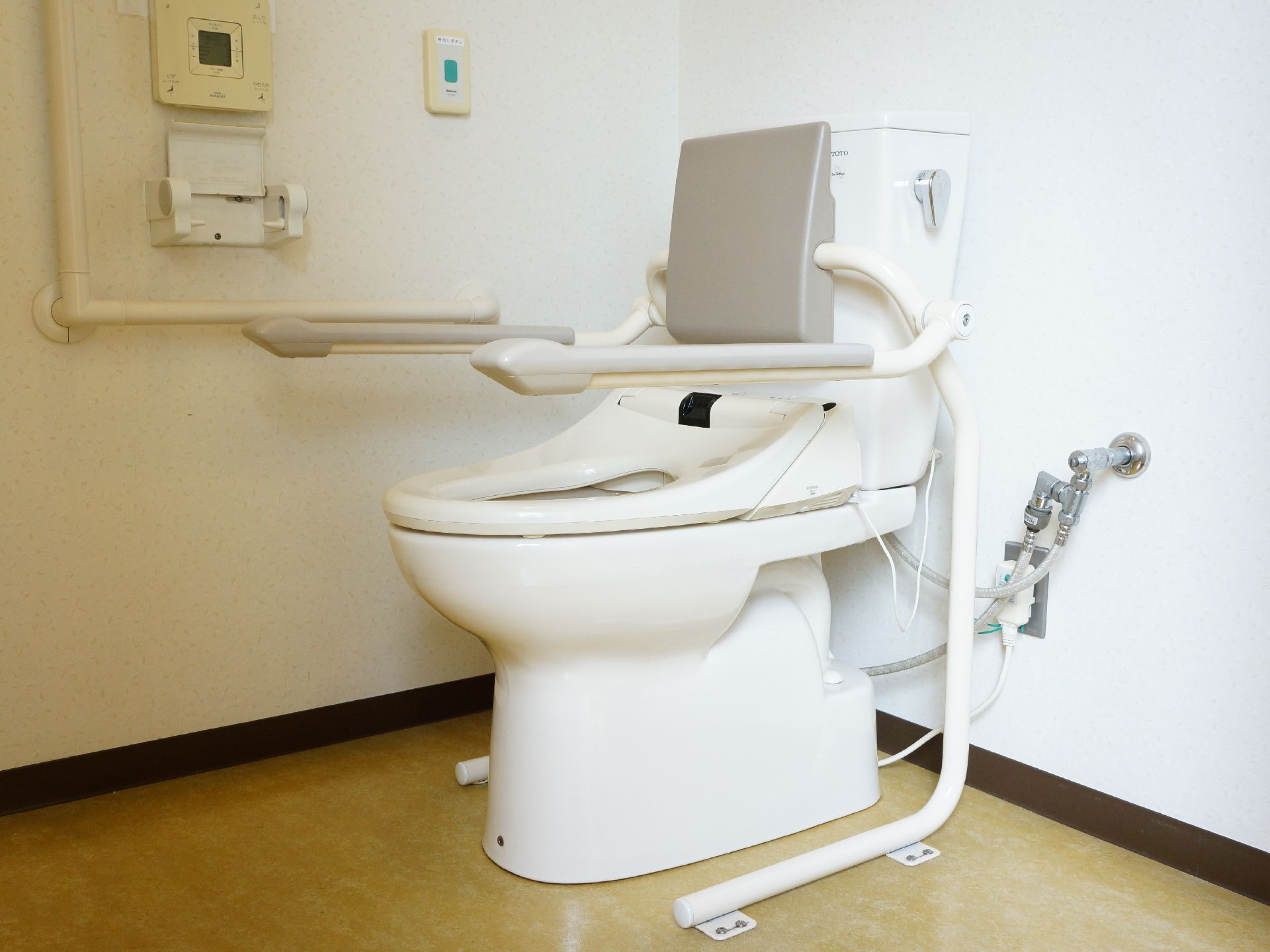トイレの壁にはL字の手すりとナースコールが付いている。温水洗浄便座付きの洋式トイレが設置され、背あてとひじ掛けが追加されている。
