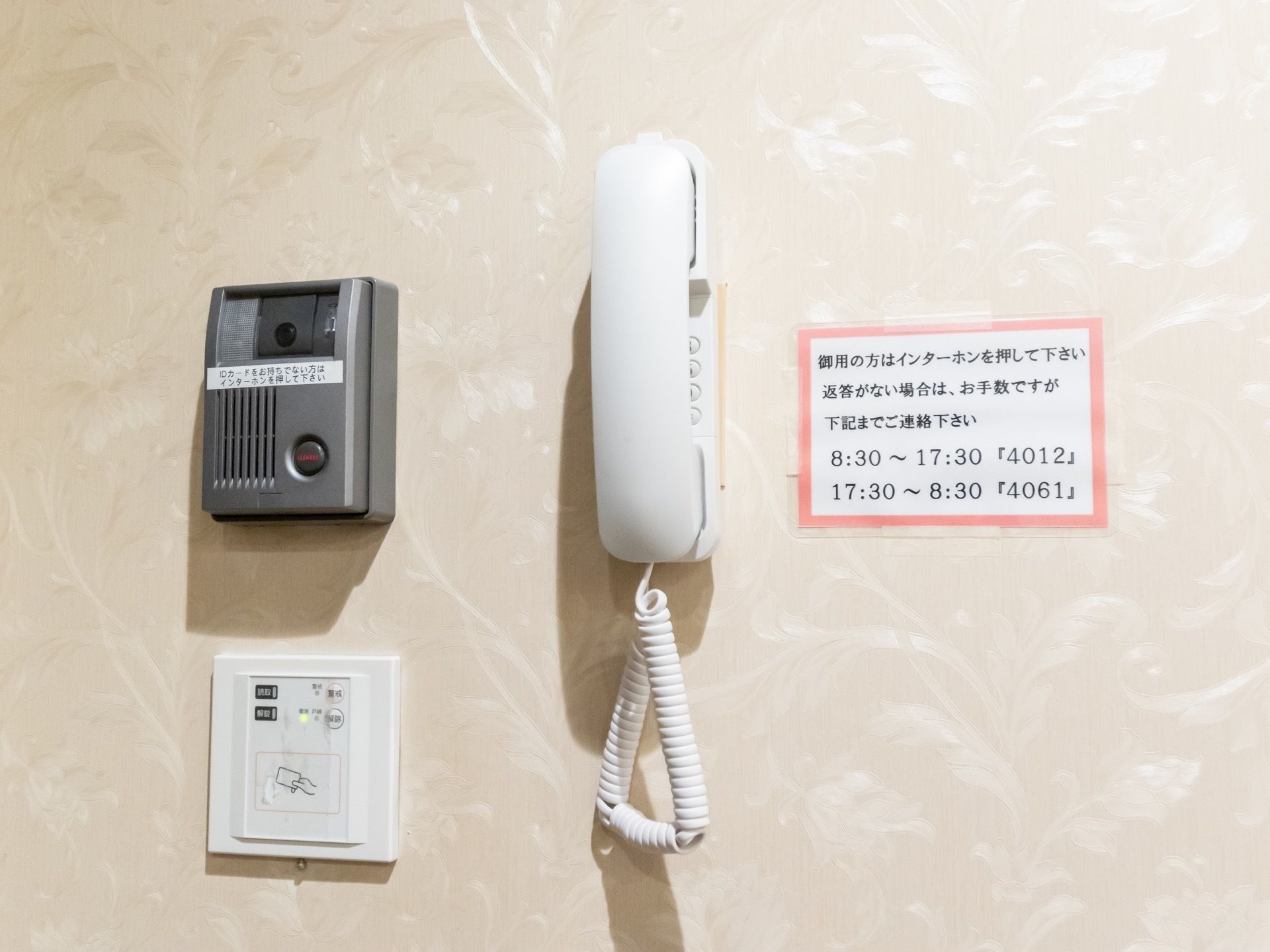 白い壁に2種類のインターホンがある。受話器の横には張り紙が貼られていて、下の方にはカードキーのようなものが付いている。
