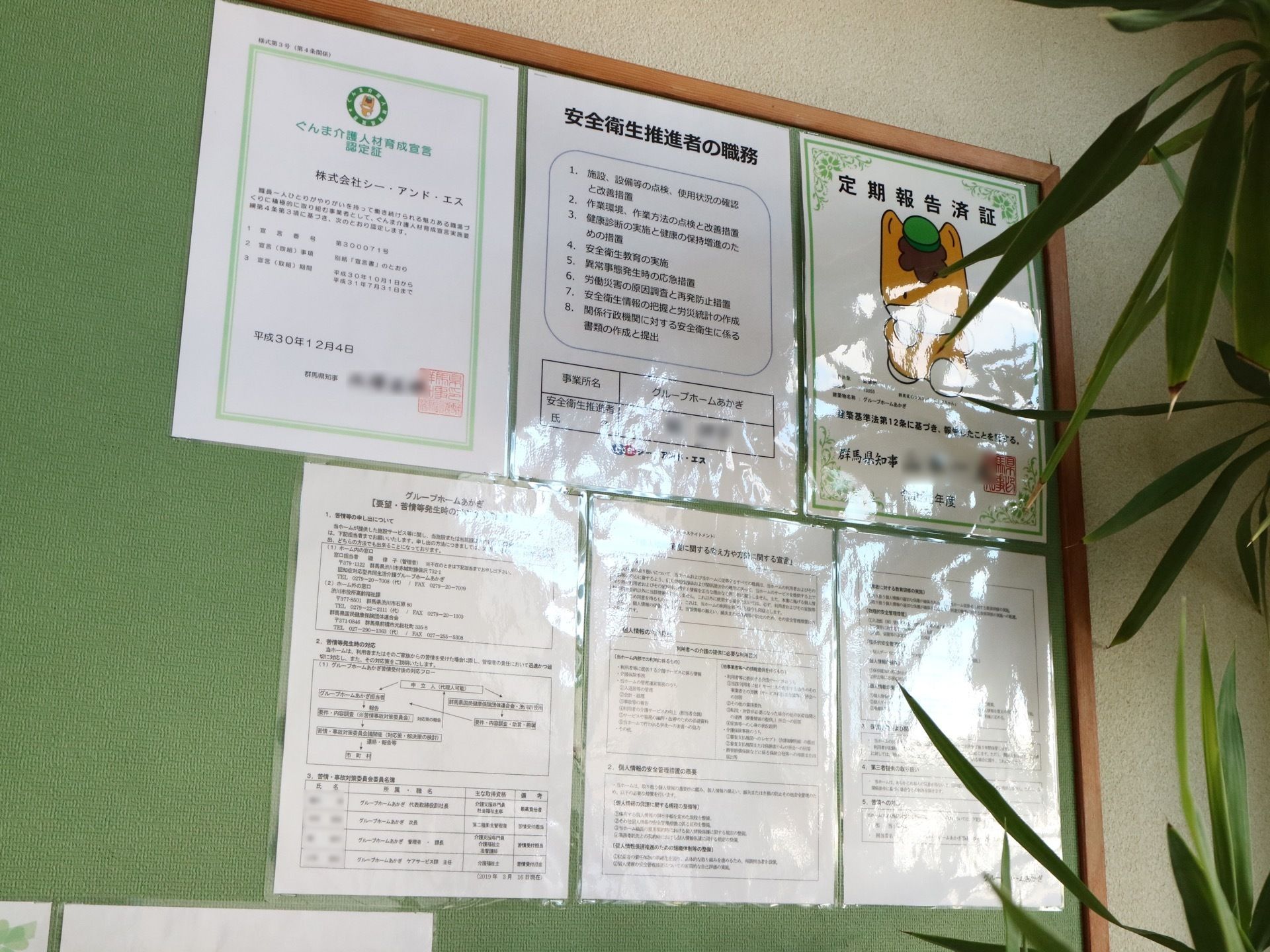 茶色い枠に緑の板の大きな掲示板が壁に設置されている。そこには、施設に関するさまざまな証明書などが貼られている。