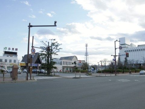 駅舎は白い外壁の建物である。整備された駅前のロータリーには何台も車が停まっている。周囲に大きな建物はない。