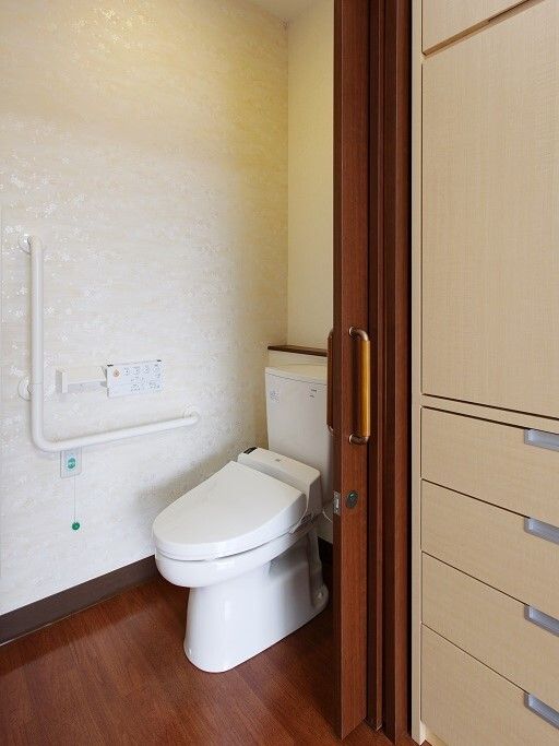 淡い色合いの花柄の壁紙が貼られた壁には、Ｌ字型の手すりや操作パネル、トイレットペーパーホルダーが設置されている。