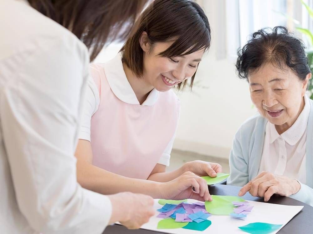 紙を貼るレクリエーションをする高齢女性と付き添いの女性ヘルパー