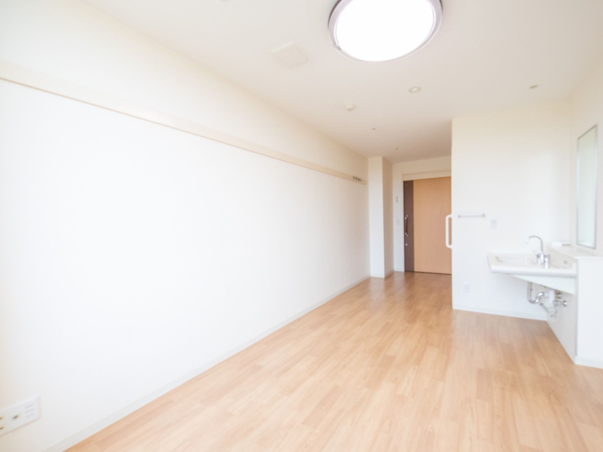 居室はフローリングとなっている。入口は引き戸で、入るとすぐ横にトイレがある。洗面台には大きな鏡が設置されている。