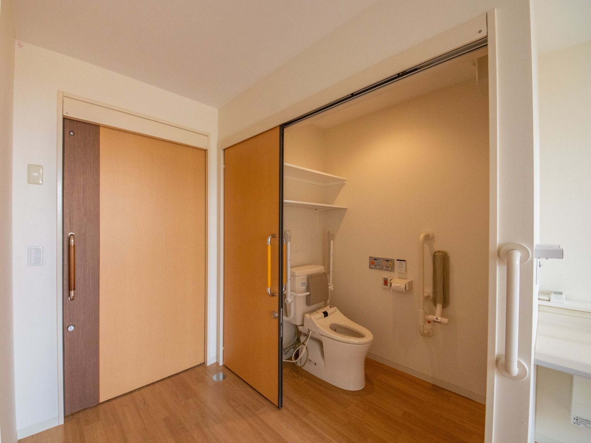 居室に入ると入口横にトイレがある。トイレは温水洗浄便座となっており、個室内には棚が２段用意されている。