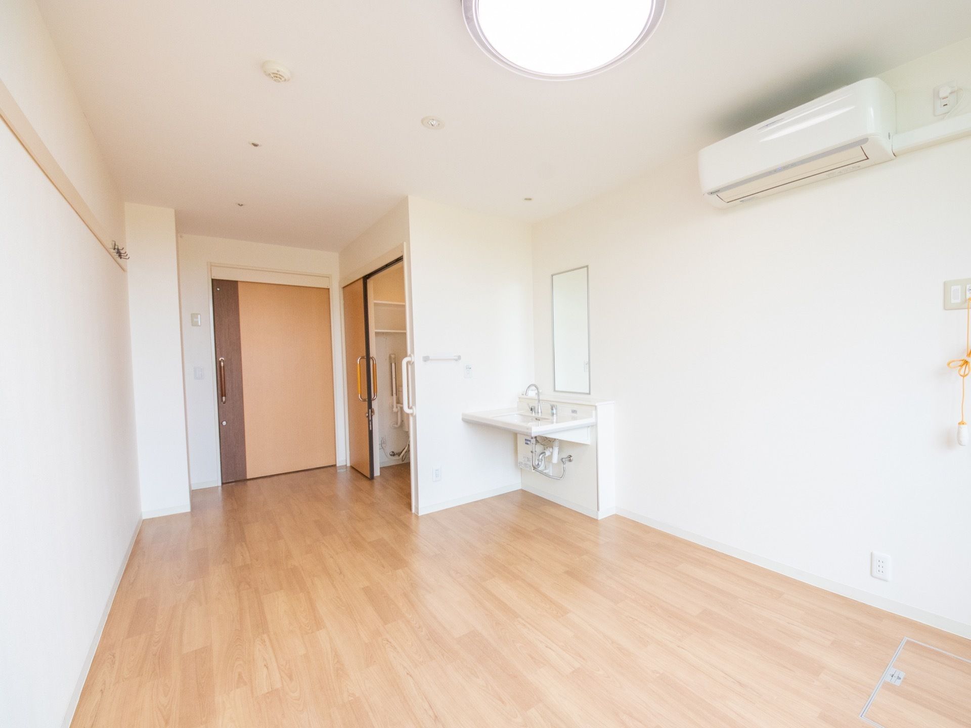 居室内を窓側から見た一例。部屋のほぼ中央にエアコンが設置されている。部屋全体がフローリングとなっている。