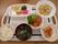 持ち手の付いたトレーの上に食事が並べられている。品数は豊富で特に野菜はサラダだけでなく漬け物や汁物、煮物などさまざまに調理されている。